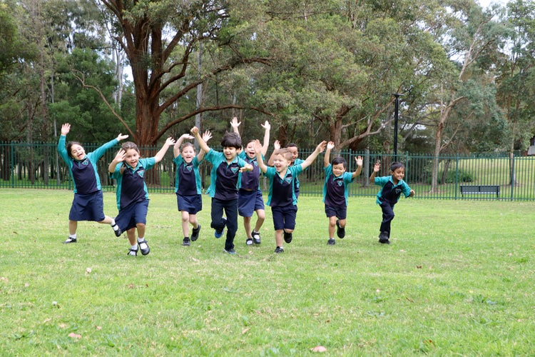 Students running across the grass oval with their hands in the air