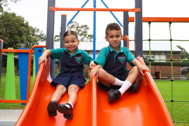 2 students sitting on the slides of play equipment