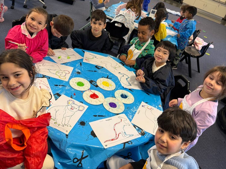A groups of smiling kindy students painting at a table