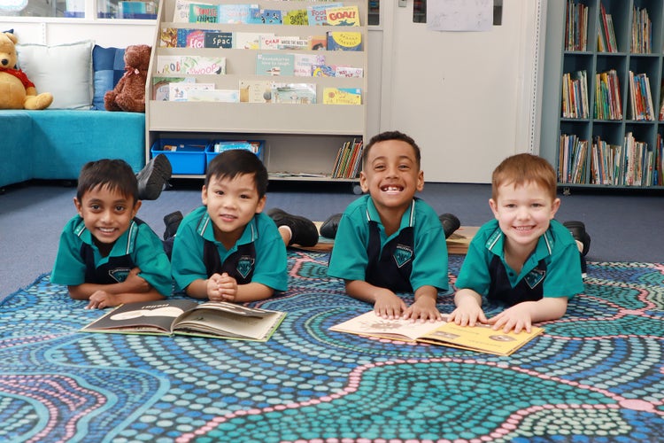 4 students lying on the floor in the library reading books together