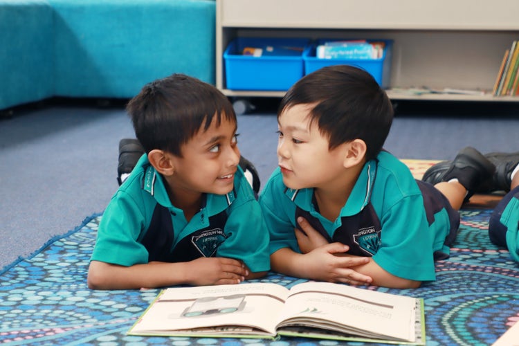 2 studnets lying on the floor reading a book