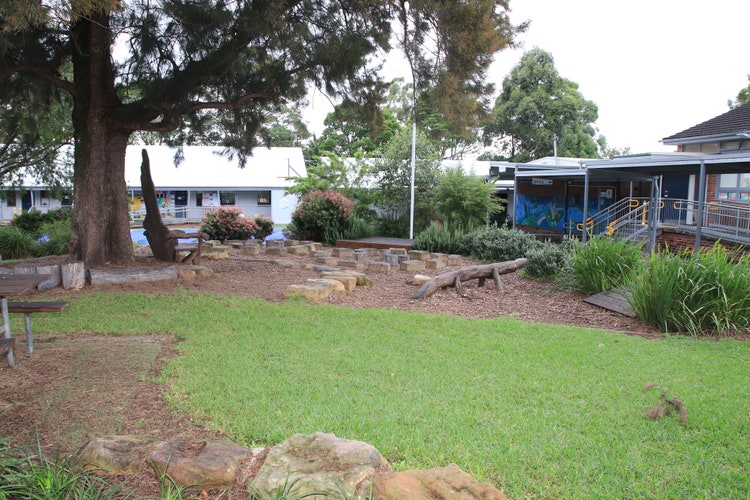Photo of school wuth buildings ni the background and green space and yarning circle.