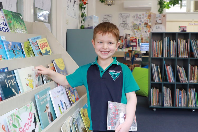 Young student selecting a book in the library, smiling.
